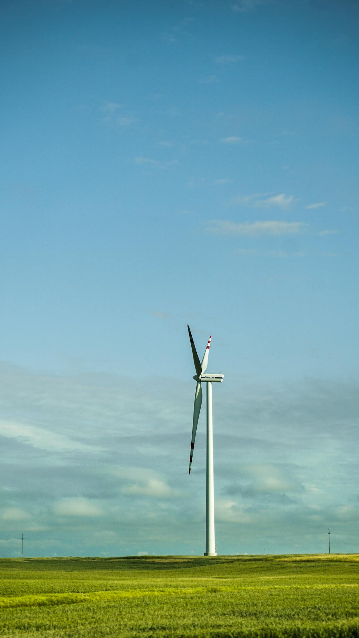 Vertical shot of a wind turbine in a vast green field under a clear blue sky, epitomizing renewable energy